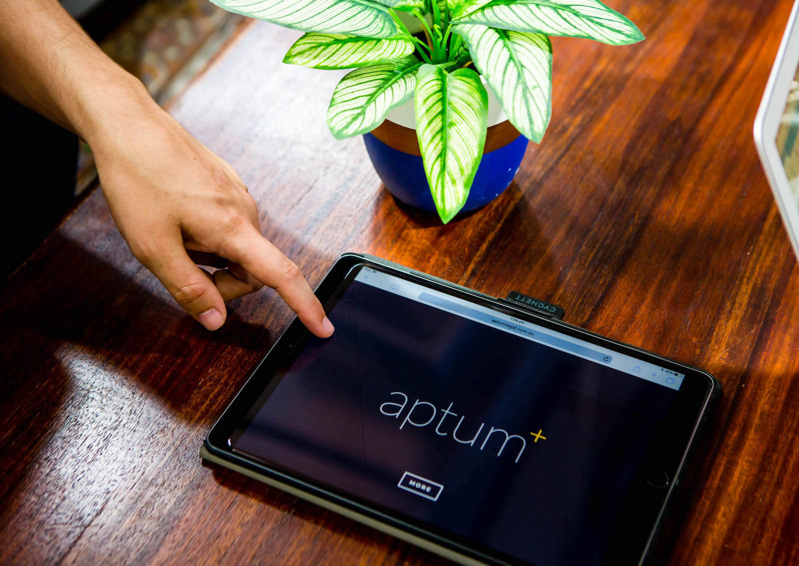 A hand points towards an ipad screen on a desk featuring the aptum logo