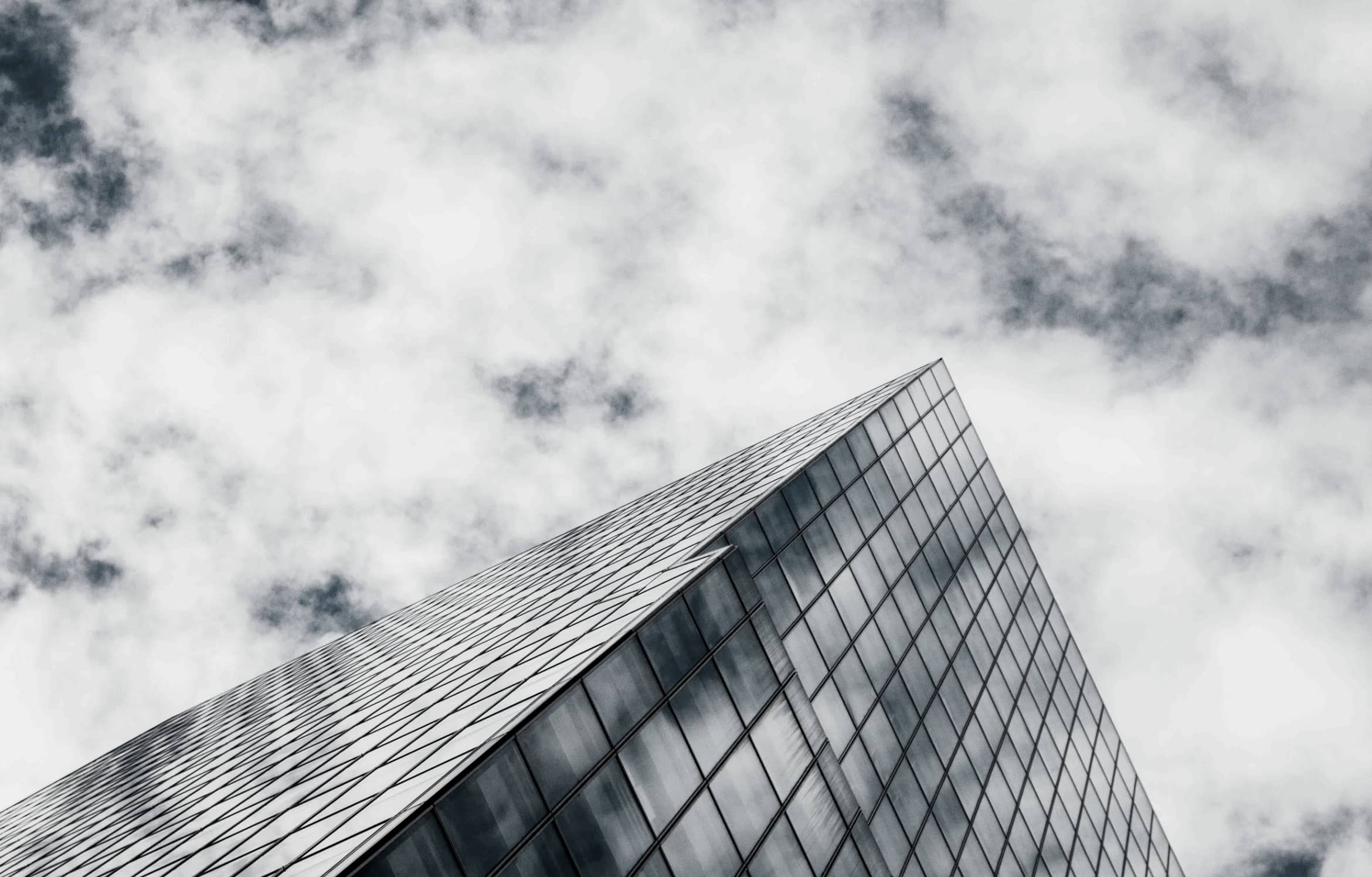 An upwards view of a glass covered office building and a cloudy sky