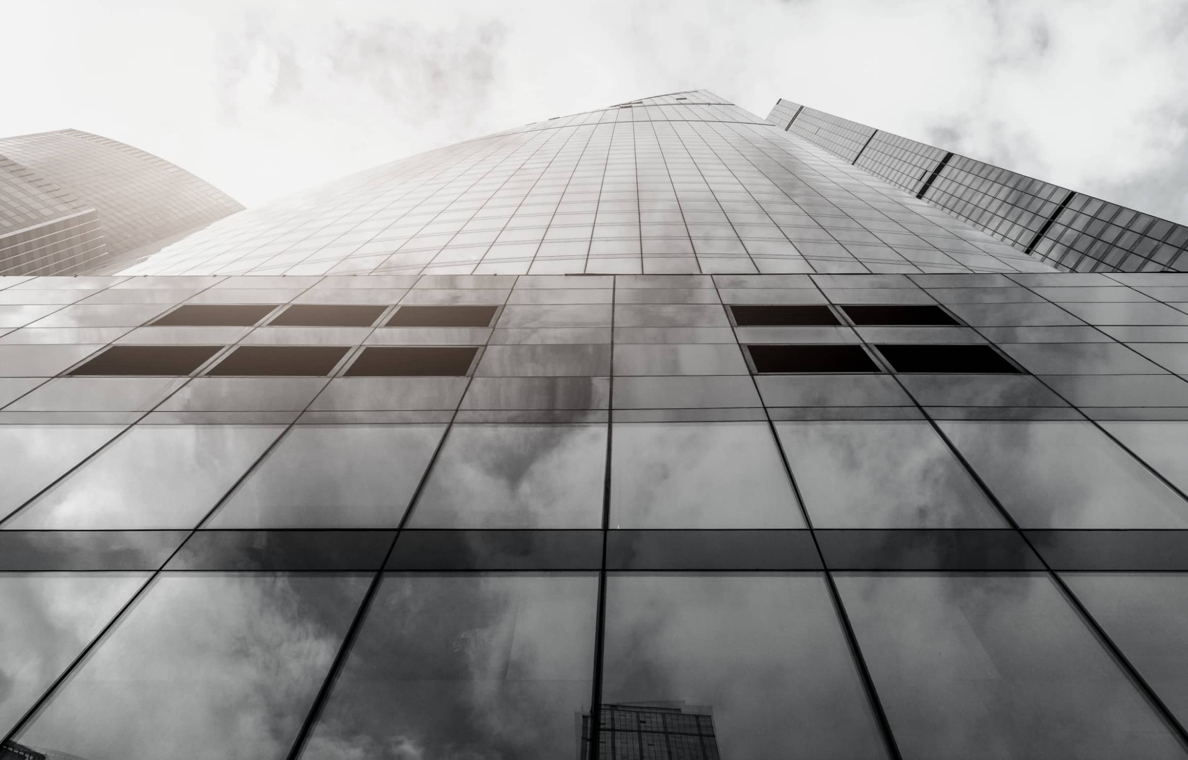 An upwards view of a glass high rise building with a cloudy sky
