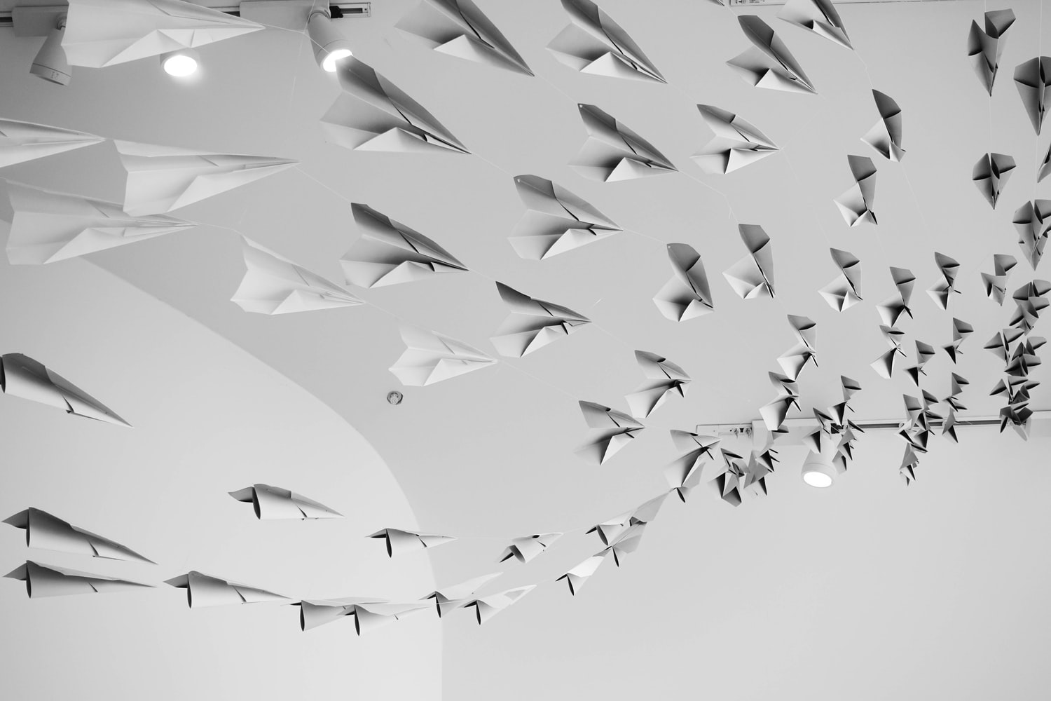 A school of paper planes flow towards a white ceiling in an open room